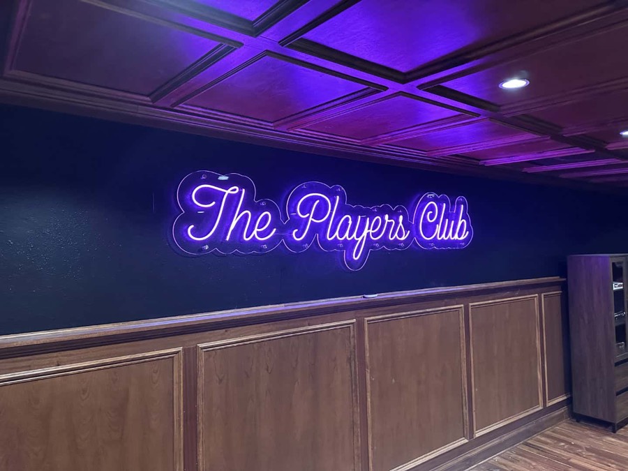 Blue neon sign reading The Players Club over a bar